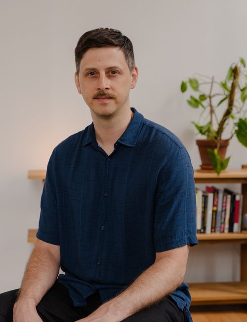 Carl, a middle aged, white man sitting in his office in front of a bookshelf with a plant and books.